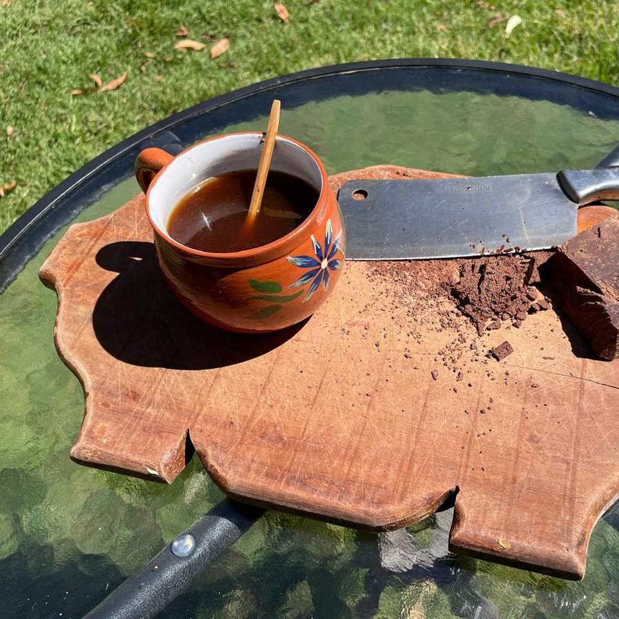 A cup of cacao beside a broken piece of a bar on a wooden board