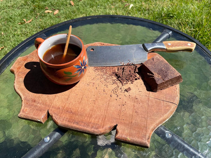 A cup of 100% Chuncho cacao with a spoon in it, on a wooden board next to a block of cacao.