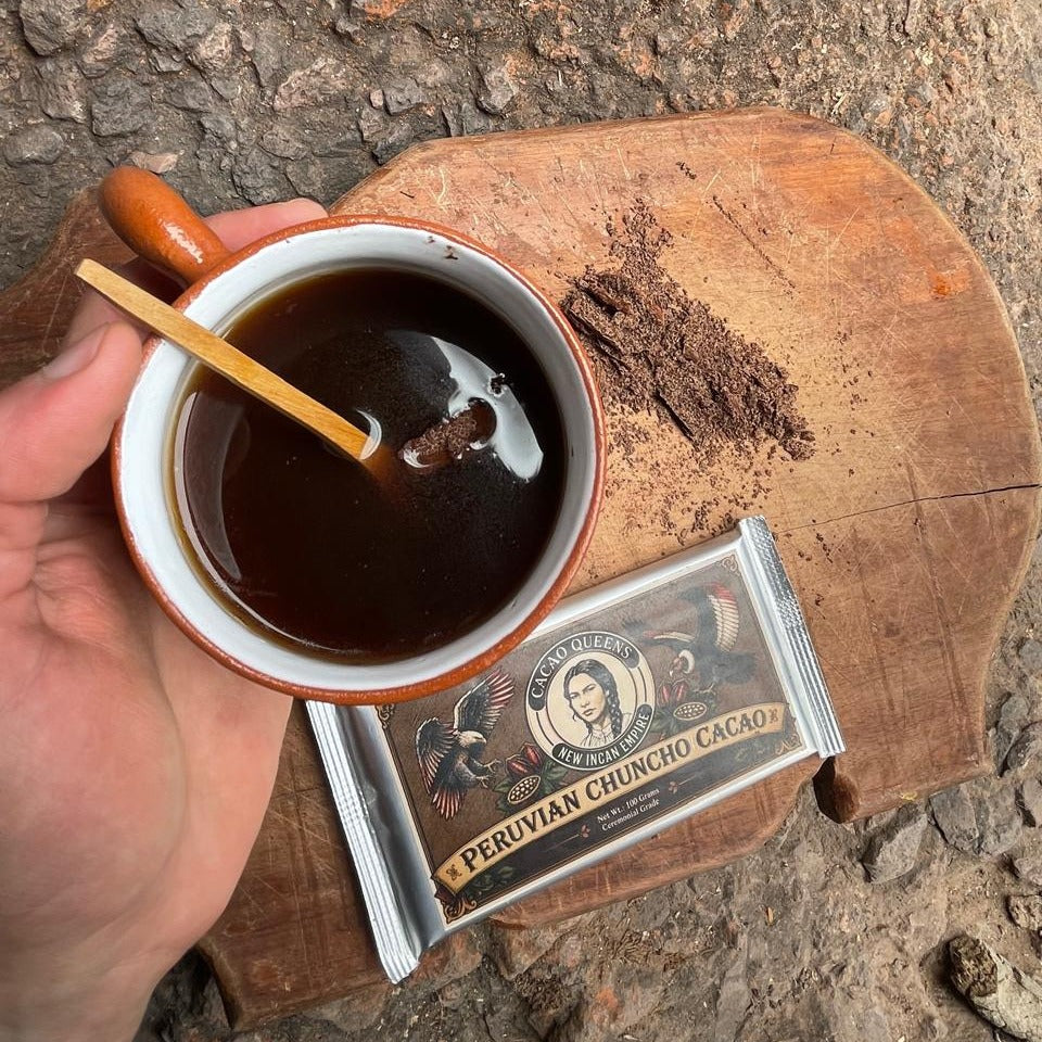 A piece of 100% Chuncho cacao melting into a cup of black coffee, with a 100 g bar beside it on a wooden board