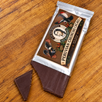 A partially unwrapped silver foil chocolate bar labeled 'Peruvian Chuncho Cacao' by Calypso Queens, placed on a wooden surface with a triangular piece of dark chocolate placed beside it.