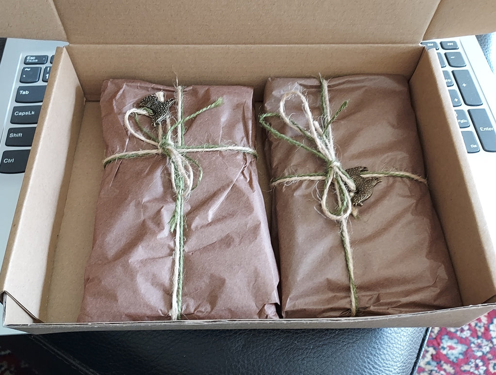 Two packages wrapped in brown kraft paper and tied with twine, placed inside an open cardboard box next to a laptop keyboard.