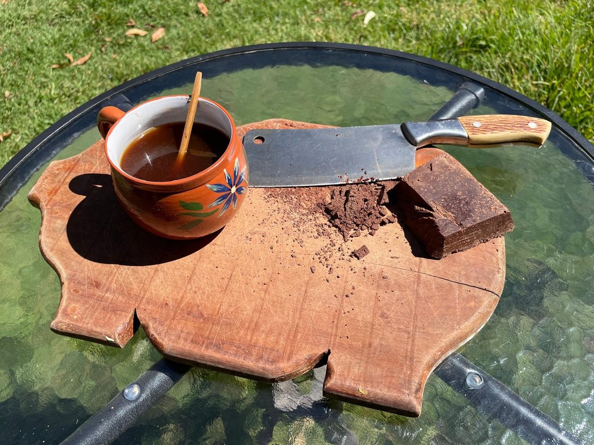 A finished cup of cacao beside a broken piece of a bar